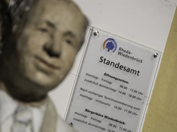 Statue vor einem Schild des Standesamts Rheda-Wiedenbrück mit Öffnungszeiten.