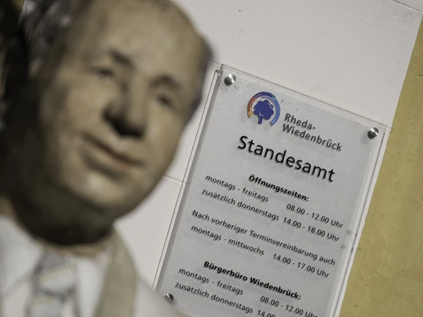 Statue vor einem Schild des Standesamts Rheda-Wiedenbrück mit Öffnungszeiten.