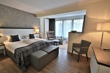 Modernes Hotelzimmer mit zwei Einzelbetten, Sitzbereich und großen Fenstern mit Tageslicht.