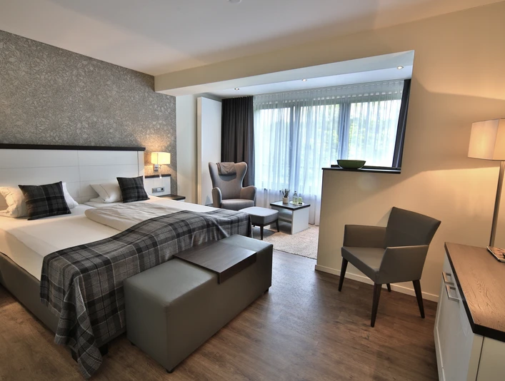 Modernes Hotelzimmer mit zwei Einzelbetten, Sitzbereich und großen Fenstern mit Tageslicht.