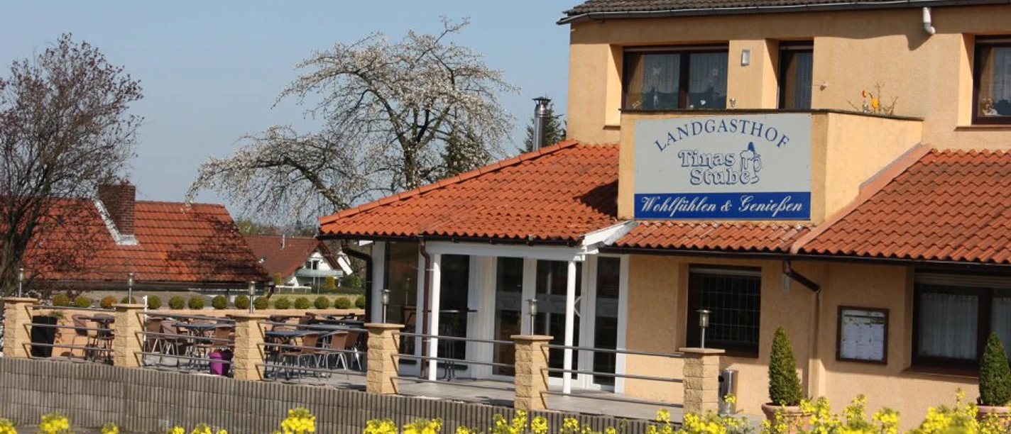 Landgasthof Tinas Stube Zweistöckiges Gebäude mit gelber Fassade und überdachtem Eingang, umgeben von blühendem Rapsfeld.