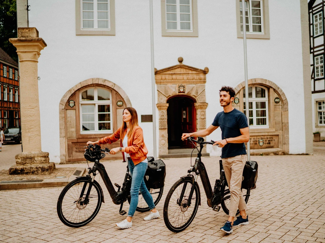 Zwei Personen mit E-Bikes stehen vor einem historischen Gebäude mit Fachwerkelementen.