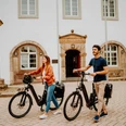 Zwei Personen mit E-Bikes stehen vor einem historischen Gebäude mit Fachwerkelementen.