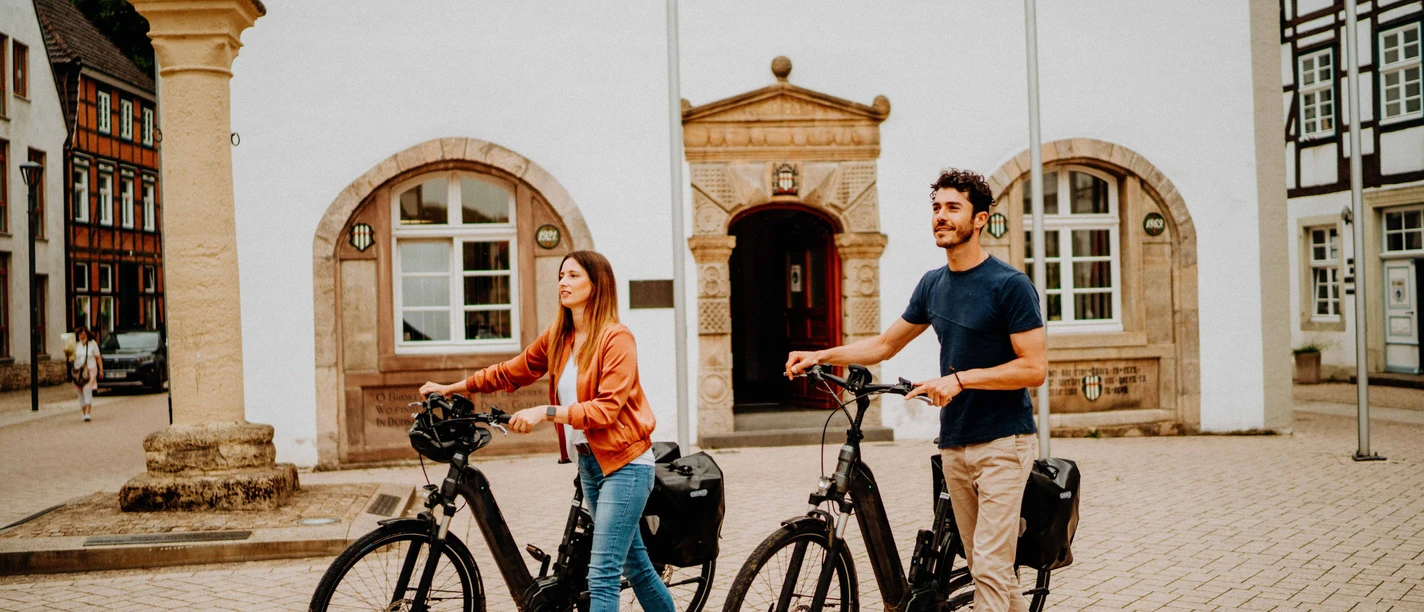 Teutoburger Wald-Brakel-Tourist Info ┬® Teutoburger Wald Tourismus (5).jpg Zwei Personen mit E-Bikes stehen vor einem historischen Gebäude mit Fachwerkelementen.