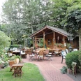 Landhotel und Restaurant zum grünen Kranze Espelkamp.png Ein Landhotel mit Restaurant, umgeben von einem einladenden, grünen Garten mit Holztischen und Stühlen.