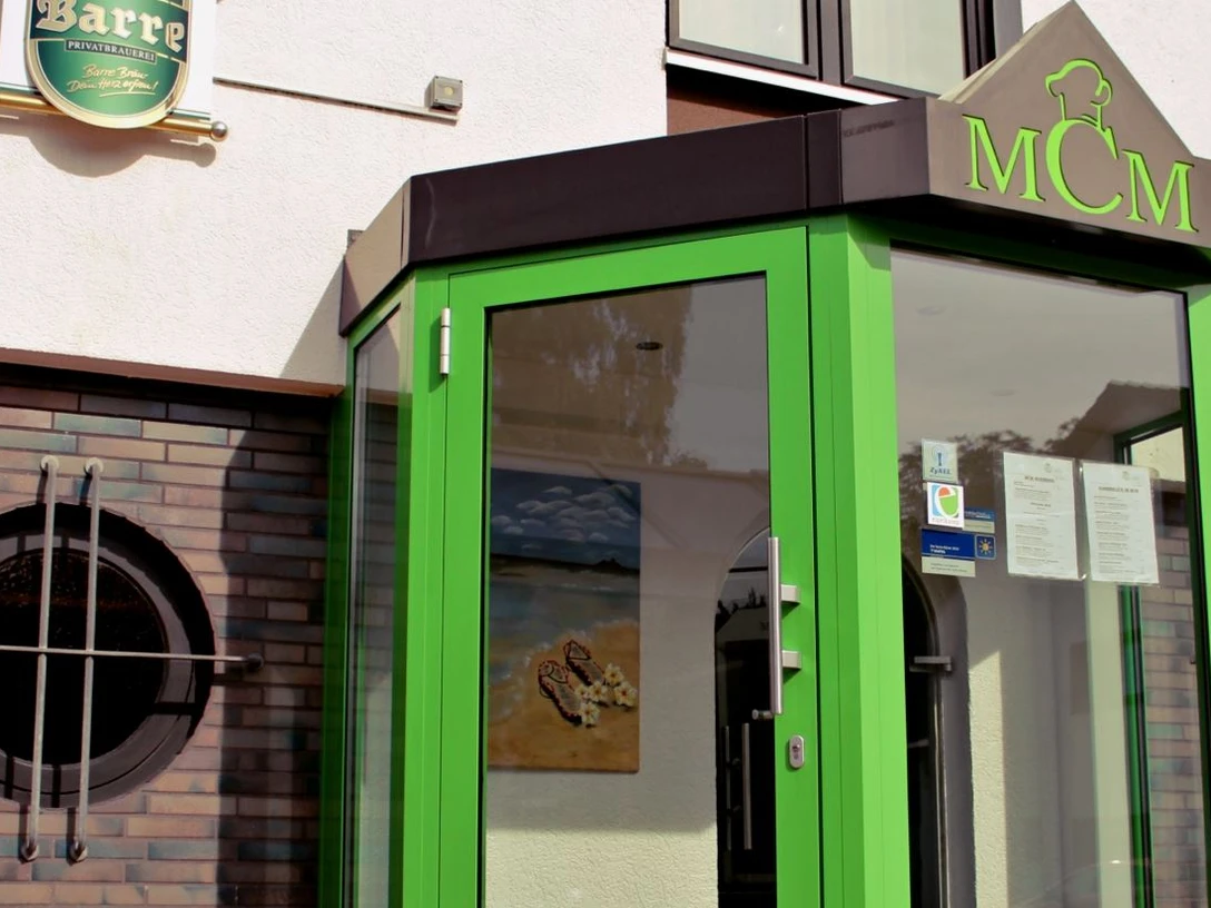 MCM Restaurant_Espelkamp.jpg Eingang des MCM Restaurants mit auffällig grünem Vordach und runden Fenstern an der Ziegelfassade.