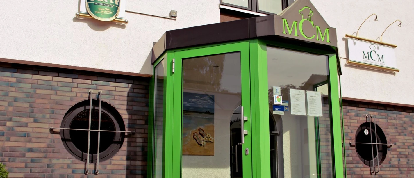 MCM Restaurant_Espelkamp.jpg Eingang des MCM Restaurants mit auffällig grünem Vordach und runden Fenstern an der Ziegelfassade.