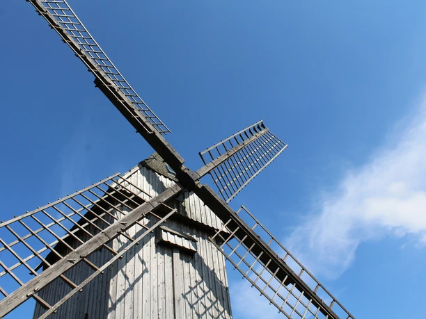 Traditionelle Bockwindmühle mit imposanten hölzernen Flügeln vor strahlend blauem Himmel.