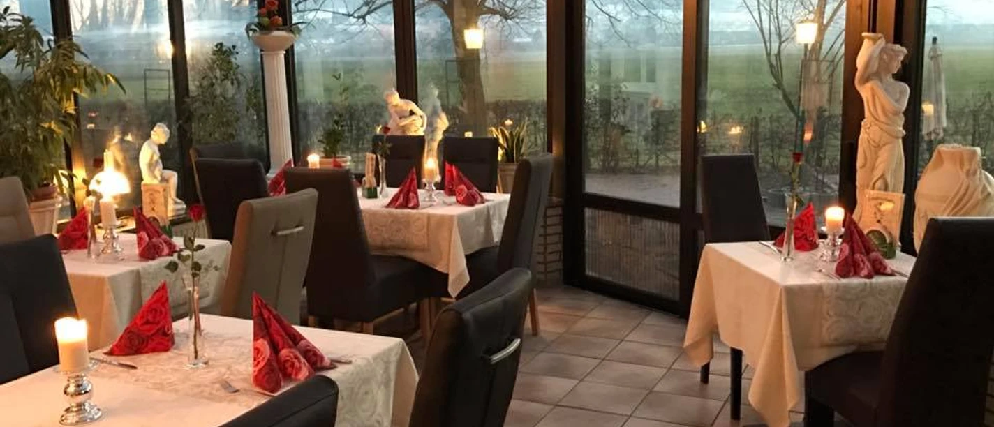 Meteora_Luebbecke.jpg Restaurant mit Glasfassade, weißen Tischdecken, roten Servietten und Kerzenlicht. Landschaft im Hintergrund.