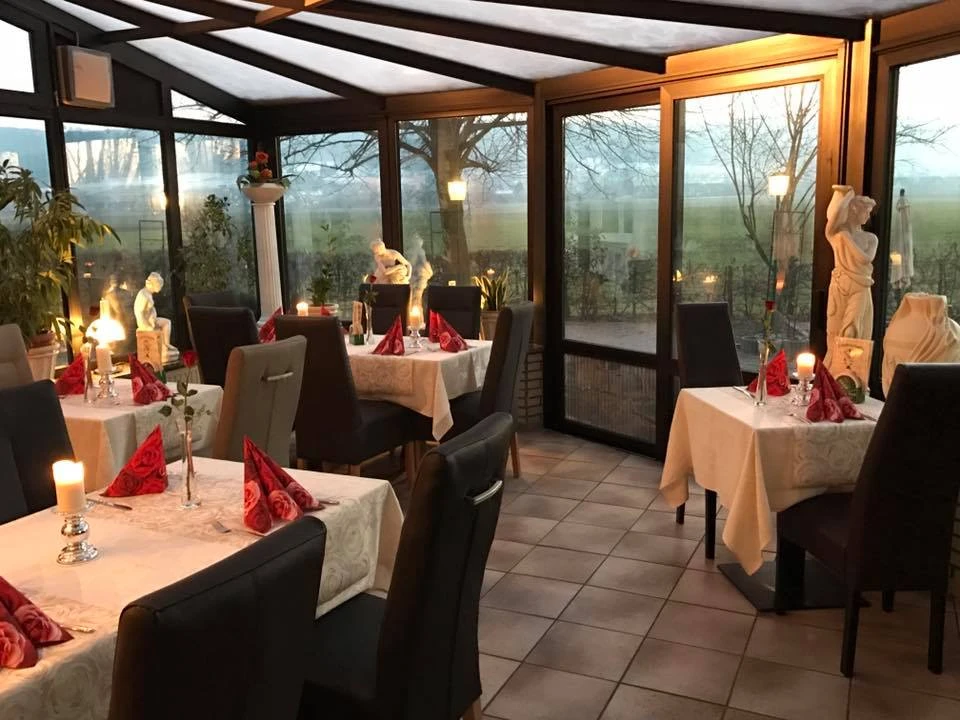 Meteora_Luebbecke.jpg Restaurant mit Glasfassade, weißen Tischdecken, roten Servietten und Kerzenlicht. Landschaft im Hintergrund.