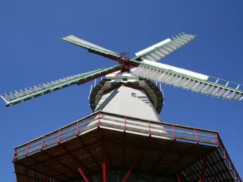 Alte Windmühle Blender vor strahlend blauem Himmel; detailreiches Flügelwerk und rotes Balkongeländer.