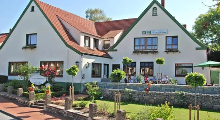 Pension "Haus Stork" Weiße Pension mit roten Dächern und grünem Zierwerk, Terrasse mit Gästen und buntem Garten.