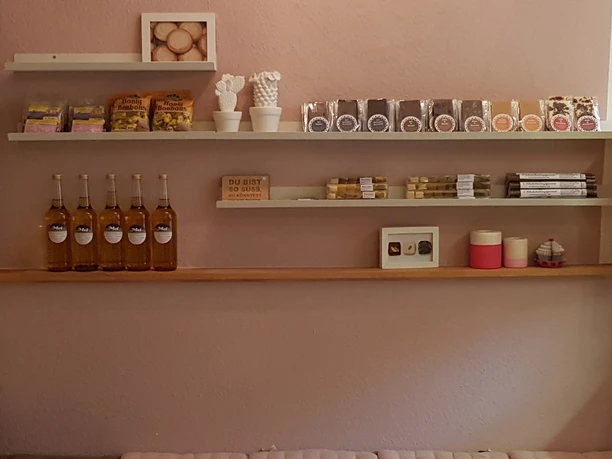 Chocolounge Laden Ein Verkaufsregal mit Produkten, darunter Honigflaschen, Schokolade, Kerzen und kleine Geschenkartikel.