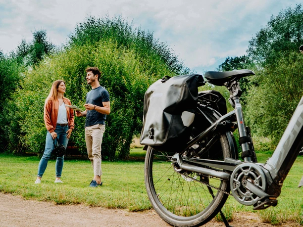 Teutoburger Wald-Brakel-Schloss Rheder ┬® Teutoburger Wald Tourismus (5).jpg Zwei Personen stehen auf einem Rasen in entspannter Unterhaltung, ein Fahrrad steht im Vordergrund.