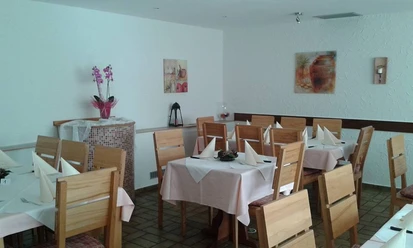 Pizzeria Bella Puglia_PrOldendorf.jpg Heller Gastraum mit Holzmöbeln, weißen Tischdecken und Dekorationen an den Wänden, einladende Atmosphäre.