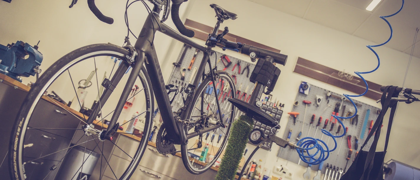 Fahrradreparatur.jpg Ein modernes Fahrrad steht auf einer Montagerampe in einer gut ausgestatteten Fahrradwerkstatt.