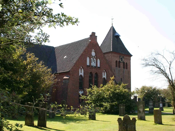 Ziegelkirche mit Spitzdach und markantem Turm, umgeben von Bäumen und alten Grabsteinen.