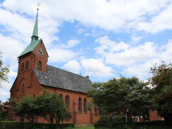 Backsteinkirche Bartholomäus in ländlicher Umgebung, grüner Kirchturm, blauer Himmel mit Wolken.