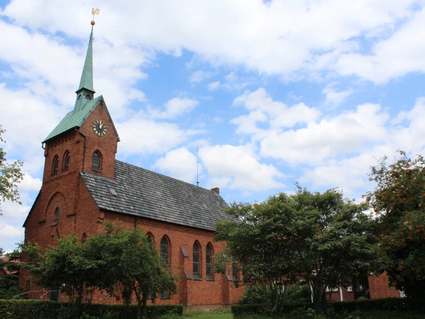 Bartholomäus-Kirche Backsteinkirche Bartholomäus in ländlicher Umgebung, grüner Kirchturm, blauer Himmel mit Wolken.