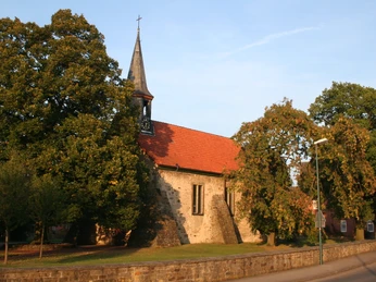Eine historische Kirche mit rotem Ziegeldach und Glockenturm, flankiert von grünen Bäumen.
