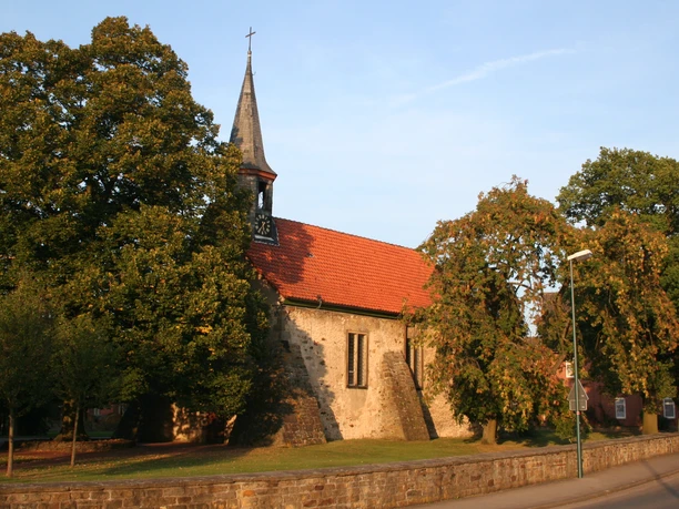 Eine historische Kirche mit rotem Ziegeldach und Glockenturm, flankiert von grünen Bäumen.