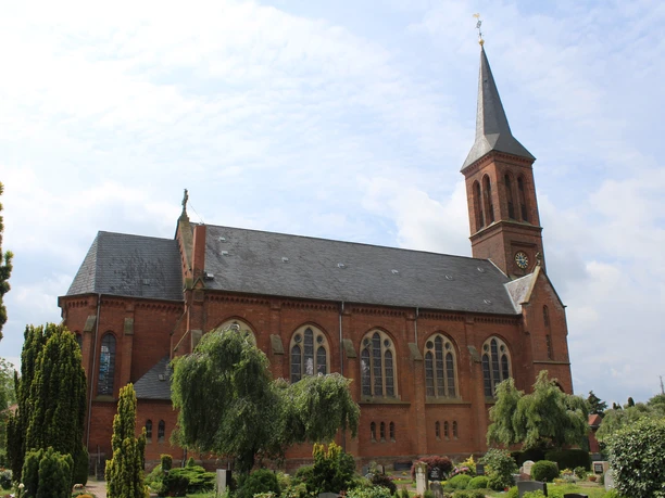 Backsteinkirche in Thedinghausen mit hohem, spitz zulaufendem Turm, umgeben von Grünflächen.