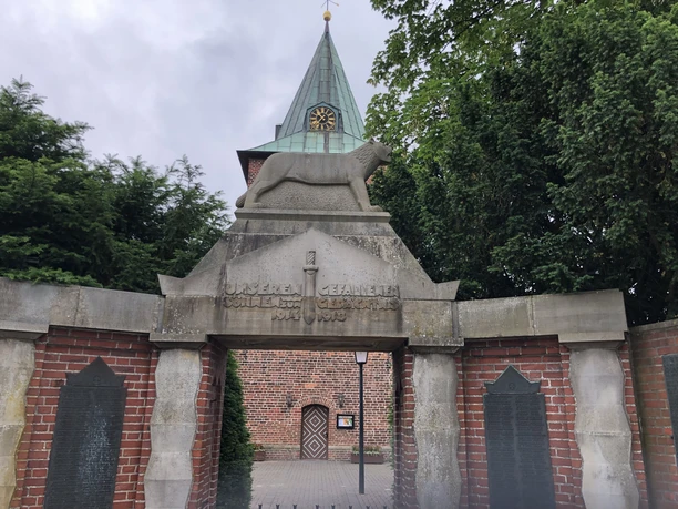 Denkmal f. d. Gefallenen und Vermissten des 1.u.2. Weltkrieges Denkmal aus Stein mit Löwenfigur und Inschrift für Gefallene beider Weltkriege, Kirche im Hintergrund.