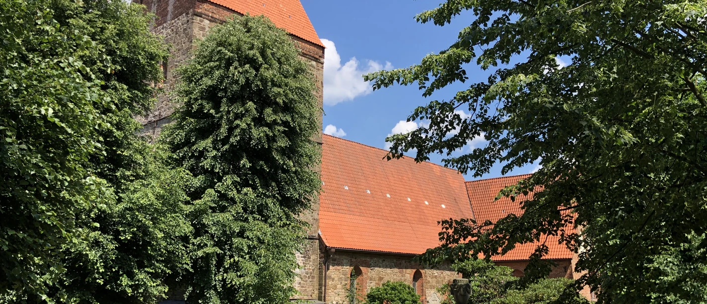 Kirche Vilsen A historic church with a red-tiled roof and tower, surrounded by trees, under a blue sky.