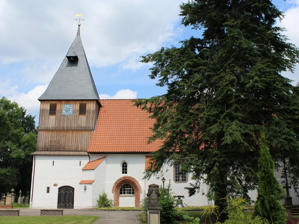 Historische Kirche in Steyerberg mit markantem Holzturm und roten Ziegeldach, umgeben von Grün.