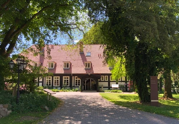 A half-timbered hotel in the countryside, surrounded by trees, with a paved path to the entrance.