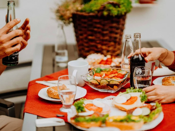 Teutoburger Wald-Brakel-Tourist Info ┬® Teutoburger Wald Tourismus (4).jpg Mehrere Personen genießen ein reichhaltiges Frühstück im Freien mit belegten Brötchen und Getränken.