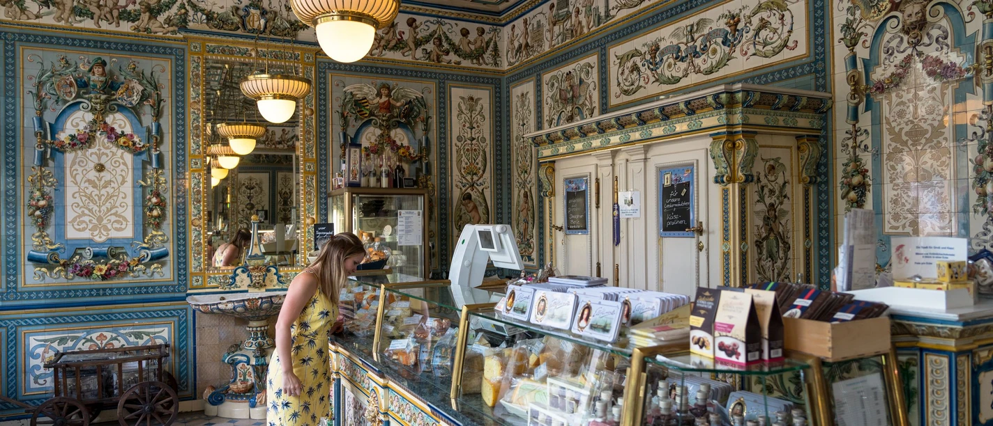 Pfunds Molkerei Eine Frau betrachtet Delikatessen in einem kunstvoll verzierten Geschäft mit reich verzierten Wänden.