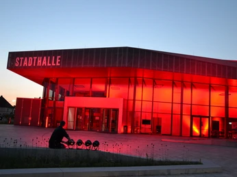 Stadthalle Night of light Die Stadthalle bei Abenddämmerung, beleuchtet in intensivem Rot, mit einem Mann im Vordergrund.