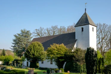 Autobahnkirche Exter, weißer Bau mit dunklem Tonnendach, umgeben von grünen Bäumen und Sträuchern.