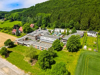 Luftaufnahme einer großen Therme umgeben von grünen Wiesen und Wäldern im Hintergrund.