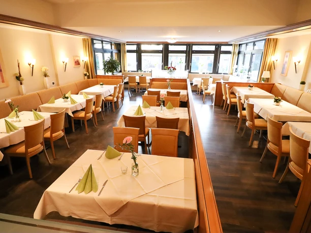 Großzügiger Speiseraum mit hellen Holzmöbeln, weißen Tischdecken und gefalteten grünen Servietten.