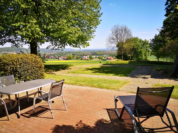 Wiehen Therme Terrasse mit Tisch und Stühlen im Vordergrund, bietet Blick auf eine grüne Landschaft und entfernte Hügel.