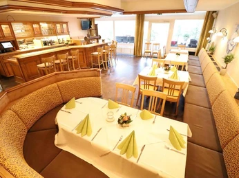 Restaurant mit gedeckten Tischen, braunen Sitzbänken, gelben Stühlen und einer Theke mit Barhockern.