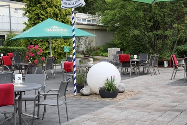 Wiehen-Therme Hüllhorst Biergarten Biergarten mit grauen Tischen und Stühlen unter grünen Schirmen, rote Polster auf den Stühlen.