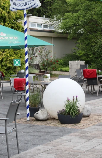 Wiehen-Therme Hüllhorst Biergarten Biergarten mit grauen Tischen und Stühlen unter grünen Schirmen, rote Polster auf den Stühlen.