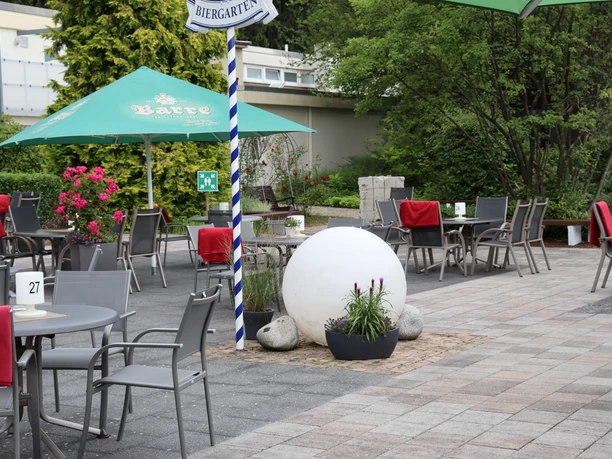 Wiehen-Therme Hüllhorst Biergarten Biergarten mit grauen Tischen und Stühlen unter grünen Schirmen, rote Polster auf den Stühlen.