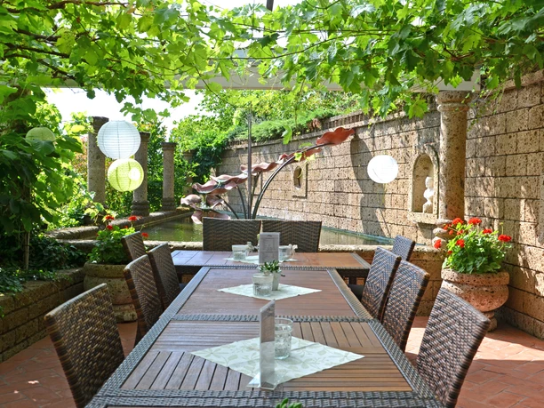 Rila erleben - Italien Ein geschmackvoll gedeckter Holztisch in einem grünen Gartenhof, umgeben von Naturpflanzen.