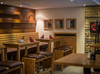 POI Schneiders am Brunnen (5 von 9)(1).jpg Holzinterieur eines Restaurants mit langen Tischen und Bänken, dezente Beleuchtung schafft eine einladende Atmosphäre.