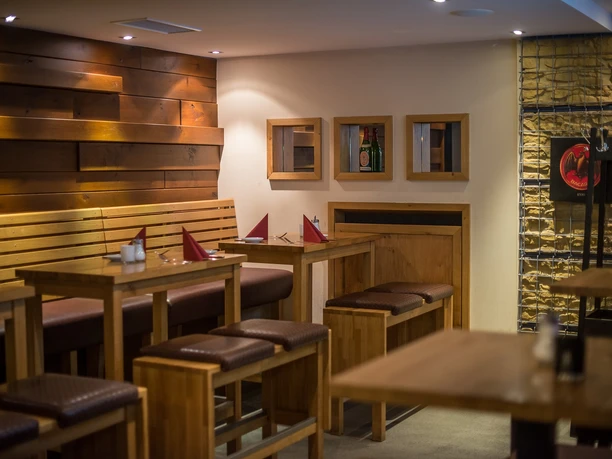 POI Schneiders am Brunnen (5 von 9)(1).jpg Holzinterieur eines Restaurants mit langen Tischen und Bänken, dezente Beleuchtung schafft eine einladende Atmosphäre.