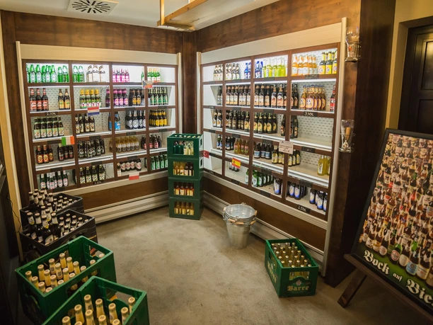 POI Schneiders am Brunnen (4 von 9)(1).jpg Ein kleiner Ladenraum voller Getränkeflaschen in Regalen und Bierkisten auf dem Boden.