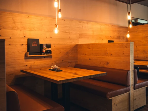 POI 5 3Steakhouse.jpg Holzverkleidete Restaurantkabine mit Lederbänken und sanfter Beleuchtung durch hängende Lampen.