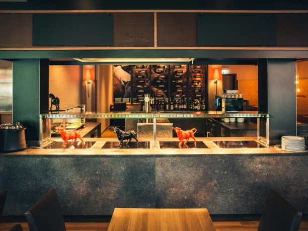 POI 3 Steakhouse.jpg Steakhouse-Innenraum mit elegantem Design, modernen Möbeln und Skulpturen von roten und schwarzen Stieren.