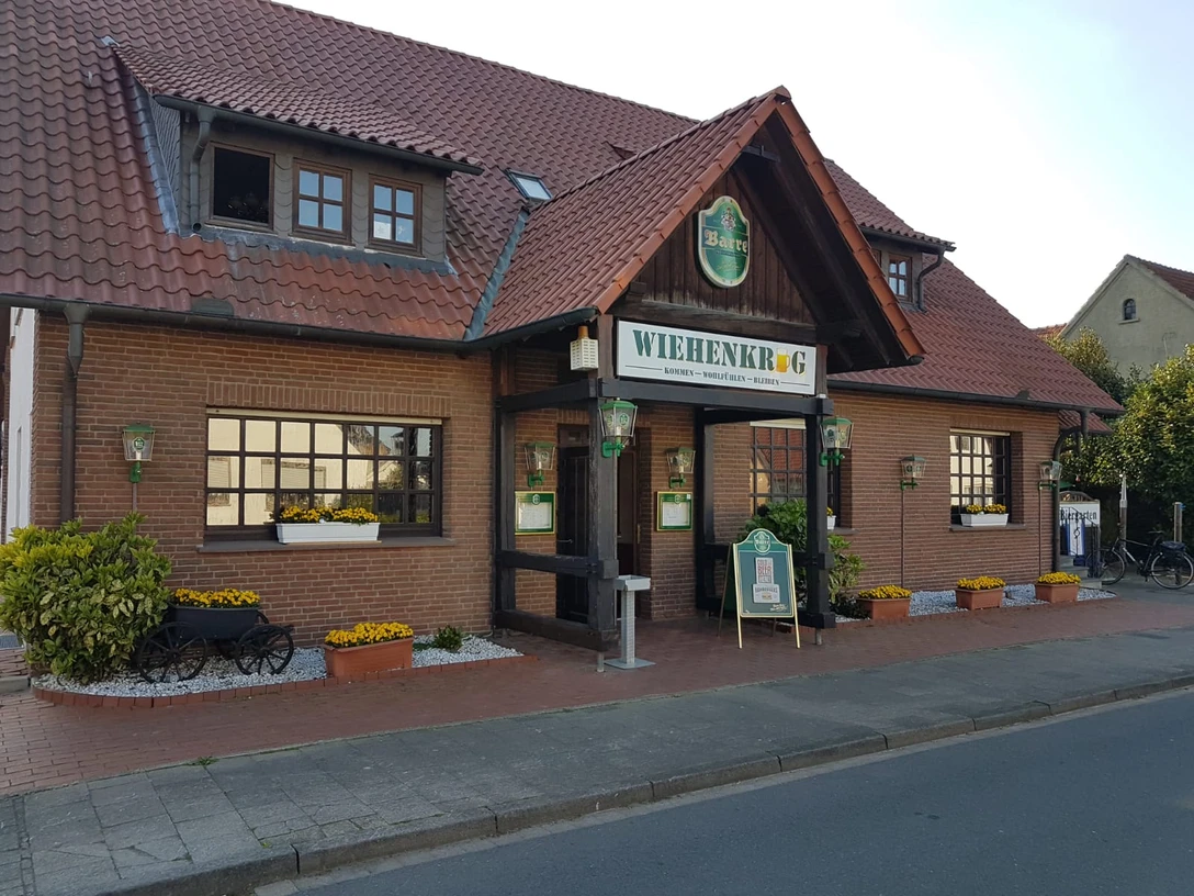 Wiehenkrug Zweistöckiges Backsteingebäude mit rotem Dach, grünen Fensterläden und einem Schild "Wiehenkrug".