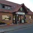 Wiehenkrug Zweistöckiges Backsteingebäude mit rotem Dach, grünen Fensterläden und einem Schild "Wiehenkrug".