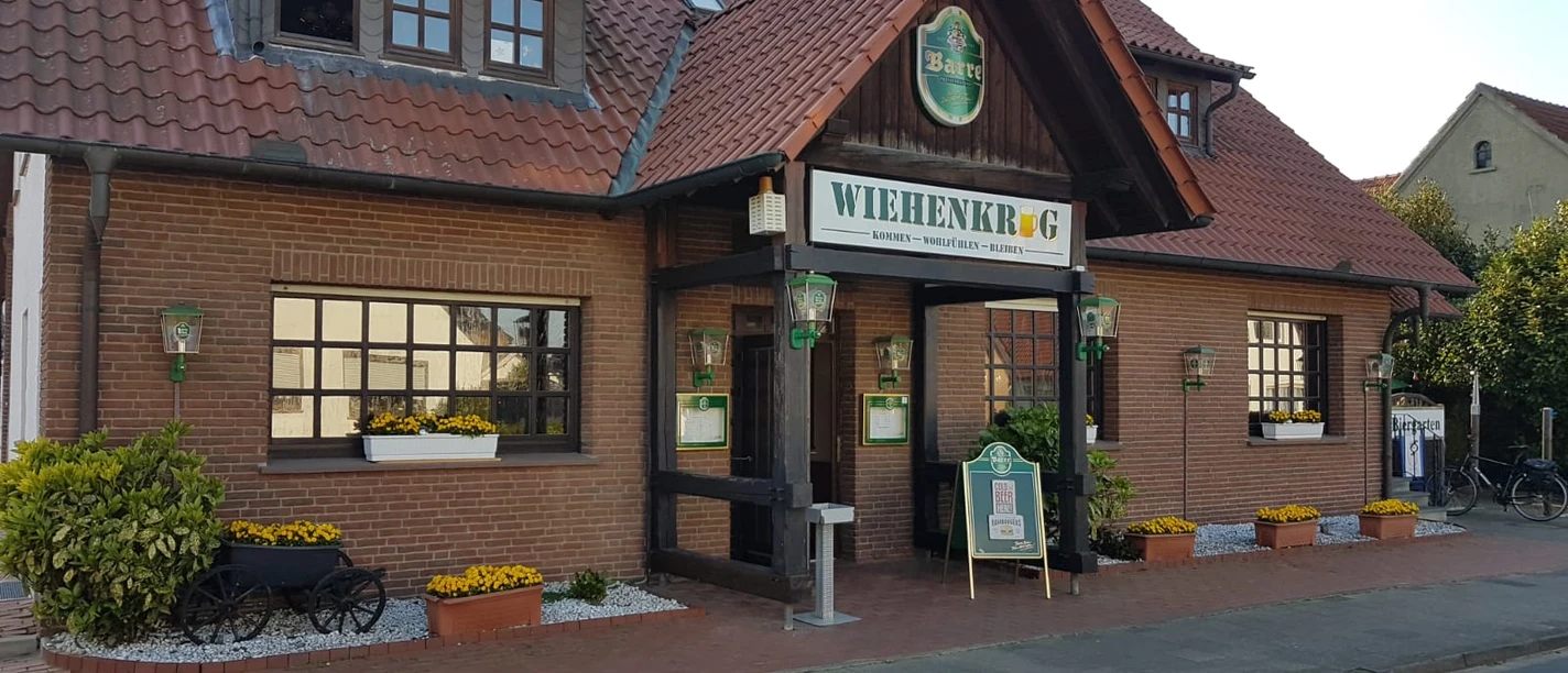 Wiehenkrug Zweistöckiges Backsteingebäude mit rotem Dach, grünen Fensterläden und einem Schild "Wiehenkrug".
